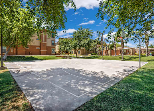 A basketball court is surrounded by trees and a building in the background. at Superstition Canyon Apartments, Apartments, Mesa, AZ
