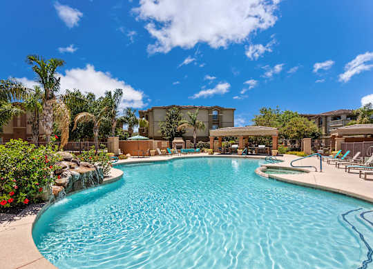 A swimming pool surrounded by palm trees and red flowers. at Superstition Canyon Apartments, Mesa, 85209