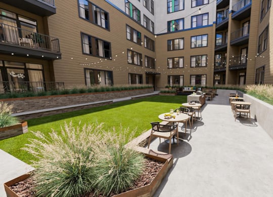 a courtyard with tables and chairs and a grassy area with a building in the background at Link Apartments NoDa 36th, North Carolina