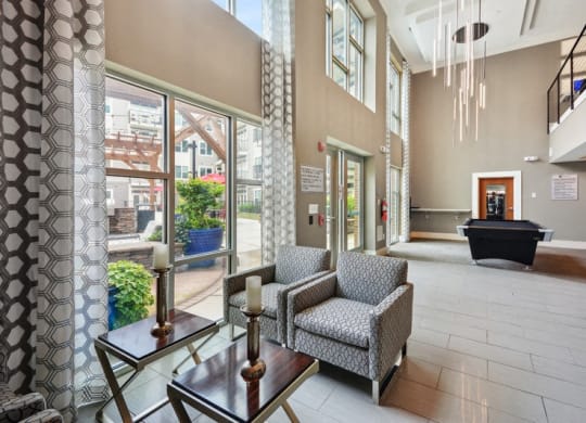 a lobby with chairs and a table in a building with large windows at Link Apartments® Brookstown, Winston Salem, NC, 27101