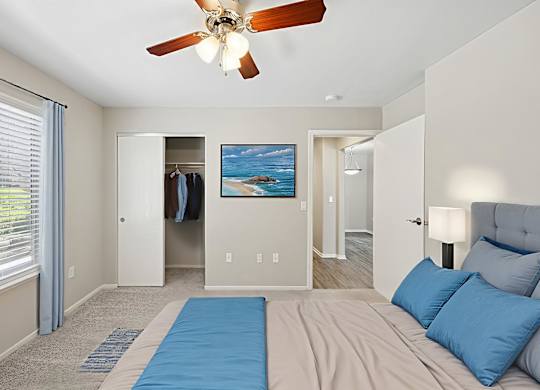A bedroom with a bed, a ceiling fan, and a painting of a beach scene on the wall.