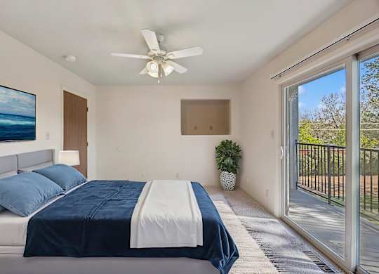 A bedroom with a bed, a ceiling fan, and a painting on the wall.