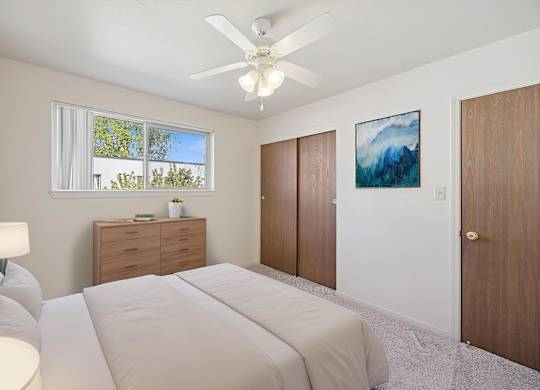 A bedroom with a large bed, a ceiling fan, and a painting on the wall.