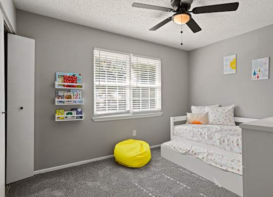 A room with a bed, a yellow bean bag chair, and a ceiling fan.