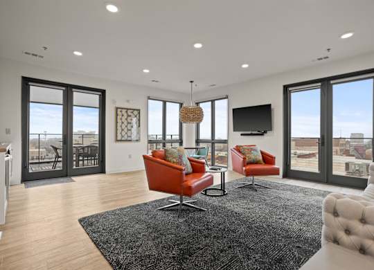 Aug Smith on Main staged modern living room on upper floor with balcony. The unit features leather chairs, carpet and a TV.
