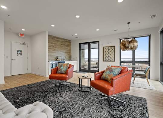 Aug Smith on Main staged living room on upper floor with balcony. The unit features leather chairs, carpet and a kitchen.