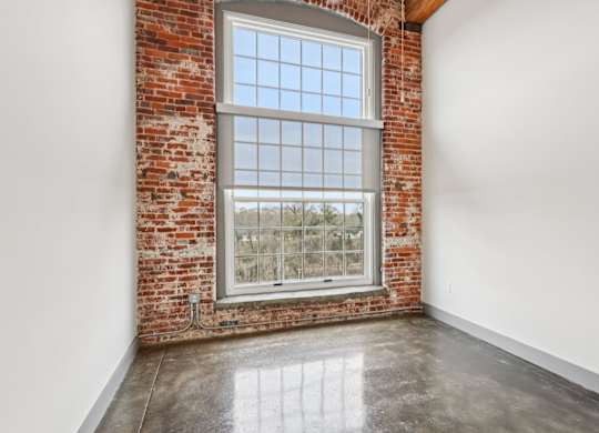Bedroom in Converse Mill Lofts in Spartanburg, SC with brick walls, high ceilings and large windows.