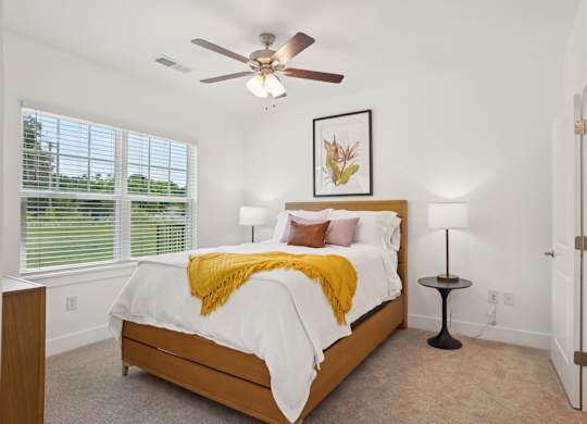 A bedroom with a bed, a ceiling fan, and a window with blinds.