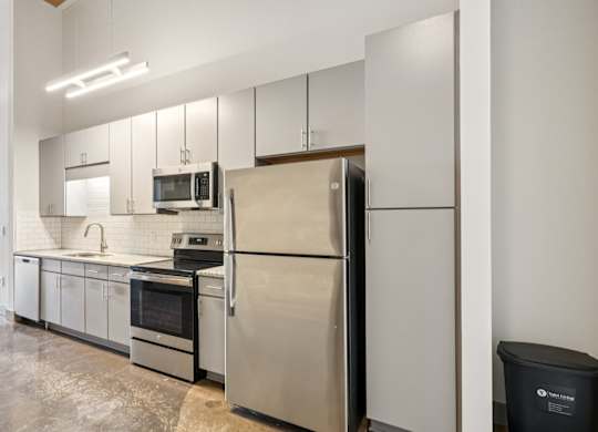 Kitchen with stainless steel appliances, granite countertops, gray cabinetry and stone floors Converse Mill Loft Apartments in Spartanburg, SC