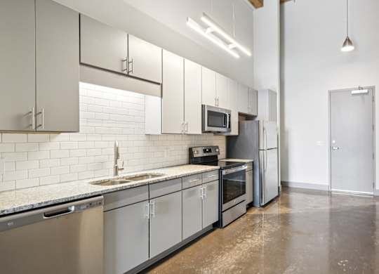 Kitchen with stainless steel appliances, granite countertops, gray cabinetry and stone floors Converse Mill Loft Apartments in Spartanburg, SC