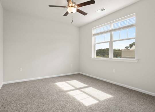 A room with a ceiling fan and a window letting in sunlight.