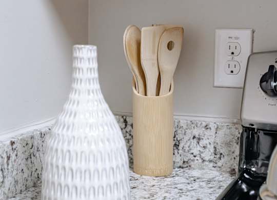 A white vase and wooden utensils are on a marble countertop.