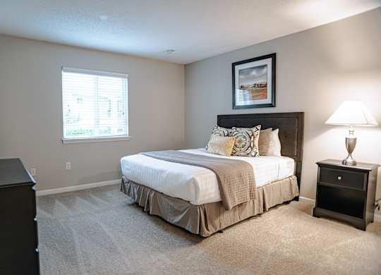 A bedroom with a large bed and a nightstand with a lamp.
