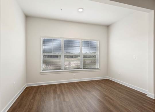 A room with a window covered by blinds and wooden flooring.