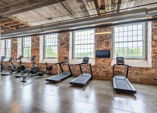 Loft Apartments for Rent in Spartanburg, SC - Converse Mill Lofts - Fitness Center with High Ceiling, Exposed Ductwork and Brick Walls, Large Windows, Large Mirror, Free Weights, and Cardio Equipment.