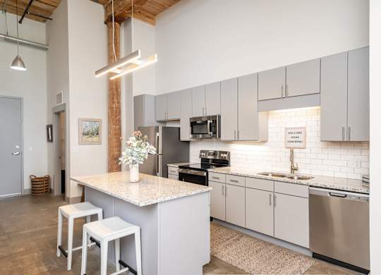 Spartanburg, SC, Loft Apartments Near Hillcrest Market Place - Converse Mill Lofts - Kitchen with Island, Custom Cabinetry, Tile Backsplash, Granite Countertops, and Stainless Steel Appliances.