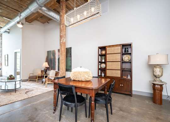Loft Apartments Near Downtown Spartanburg, SC - Converse Mill Lofts - Living Room with High Ceiling, Large Window, Chaise Lounge, Pendant Lighting, Couch, Coffee Table, Armchairs, and Paintings.