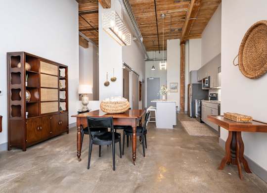 Loft Apartments Near Downtown Spartanburg, SC - Converse Mill Lofts - Living Room with High Ceiling, Large Window, Chaise Lounge, Pendant Lighting, Couch, Coffee Table, Armchairs, and Paintings.