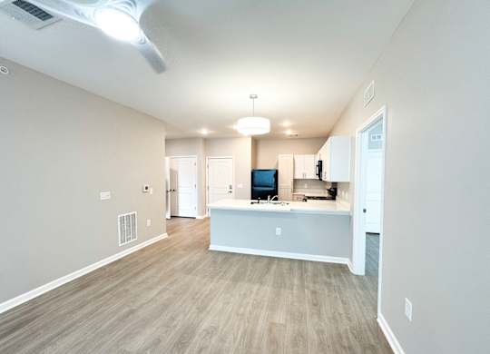 The Haven at Palmer Pointe Senior Apartments living room with luxury vinyl tile flooring, kitchen peninsula, black refrigerator and ceiling fan