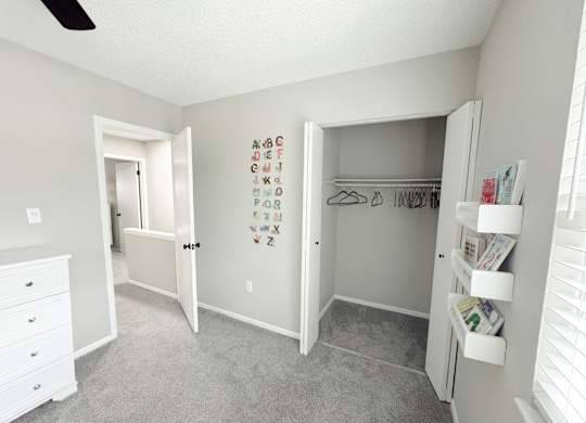 Reserve at Hillcrest child's bedroom with gray carpet, a window and sticker letters on wall and shelves with books. It also has one large, walk-in closet.
