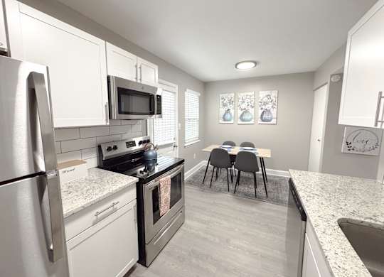 Reserve at Hillcrest Townhomes furnished kitchen with granite countertops, stainless steel appliances, and a dining room table.