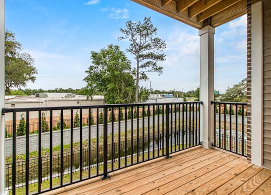 A wooden deck with a black railing and a view of a street and trees.