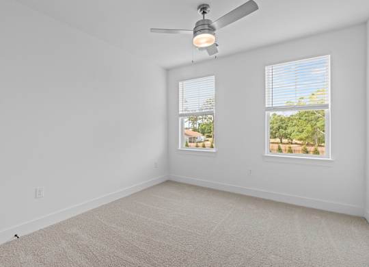A room with a ceiling fan and two windows.