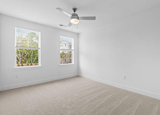 A room with a ceiling fan and two windows.