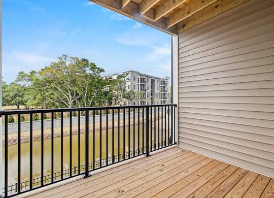 A balcony with a black railing and wooden floor overlooks a body of water and buildings.
