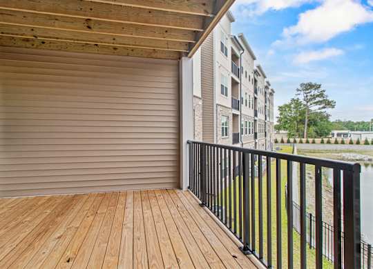 A wooden deck with a black railing and a sliding glass door leading to a balcony.