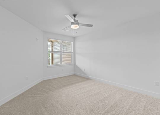 A room with a carpeted floor and a ceiling fan.