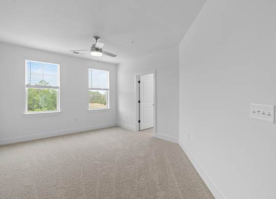 A room with a carpet floor, a ceiling fan, and a door.