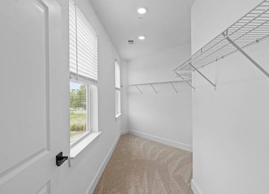 A room with a carpeted floor, a window with blinds, and a metal shelving unit.