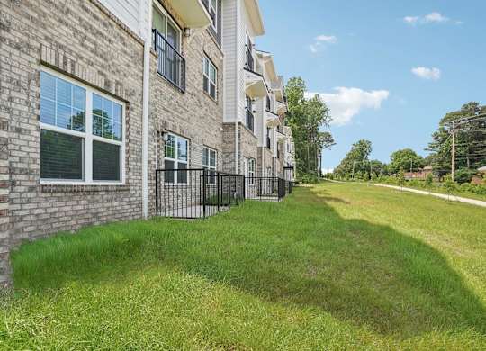 A grassy area in front of a brick building with a black fence.