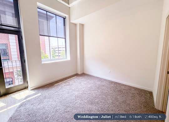A bedroom with a large window and a carpeted floor.