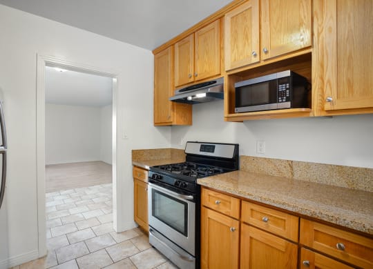 Apartment kitchen with stainless steel appliances, tan counter tops, and wood cabinets.