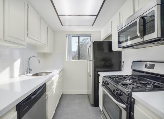 Apartment kitchen with stainless steel appliances, white tile back splash, white counter tops, and white cabinets.