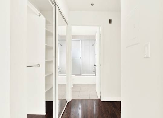 A white hallway with a door on the left and a bathroom in the distance at Peach Tree Court, Los Angeles, 90024