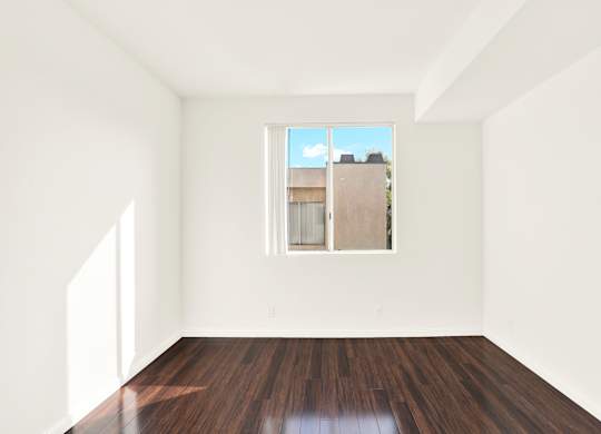 A room with wooden floors and a window showing a building outside at Peach Tree Court, Los Angeles, CA 90024