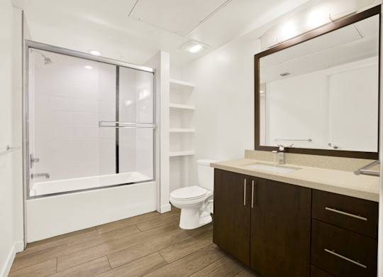 A bathroom with a toilet, sink, and a bathtub with a glass door at The Urbanpolitan, Los Angeles, 90036