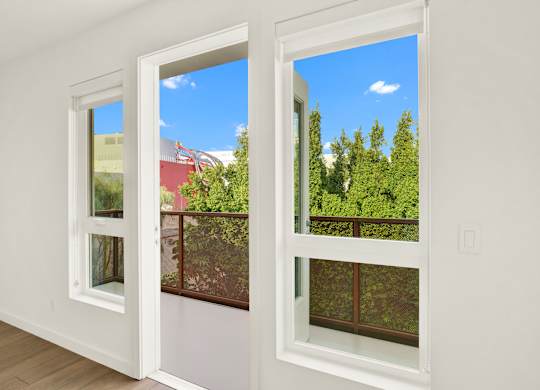 A room with two windows overlooking a red building and green trees at The Urbanpolitan, Los Angeles, CA 90036