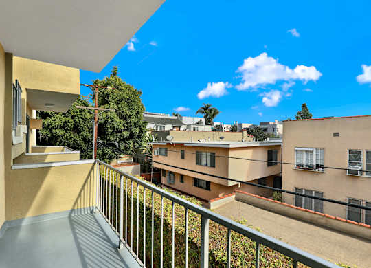 A balcony overlooks a courtyard with buildings and trees at Wooster Encore Apartments, California 90035