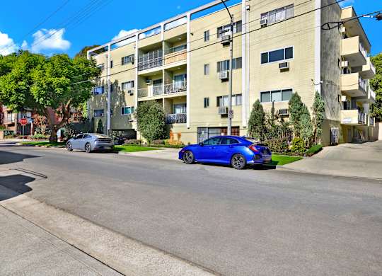 A blue car is parked on the side of a street in front of a building at Wooster Encore Apartments, California
