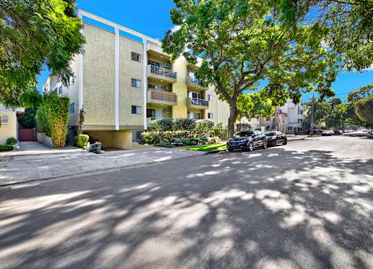 A car is parked on the street in front of a yellow building at Wooster Encore Apartments, Los Angeles, CA