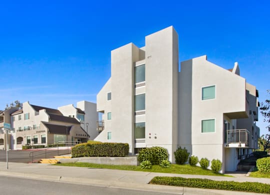 A modern building with a white facade and greenery in front.