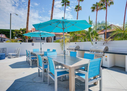 a patio with a grill and tables with blue chairs and umbrellas  at Laguna Gardens Apts., Laguna Niguel