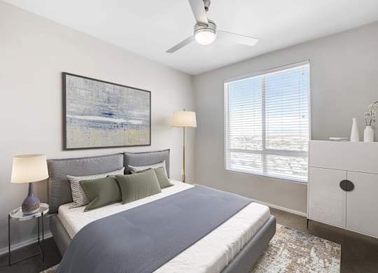 A bedroom with a bed, a nightstand with a lamp, a dresser, and a ceiling fan.