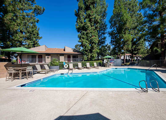 A swimming pool surrounded by trees and chairs.