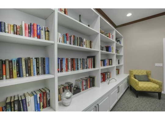 a large book shelf with many books and a yellow chair  at Tesoro Senior Apartments, Porter Ranch, CA, 91326
