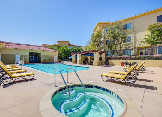 a swimming pool with a hot tub and lounge chairs with a hotel in the background  at Tesoro Senior Apartments, Porter Ranch, California